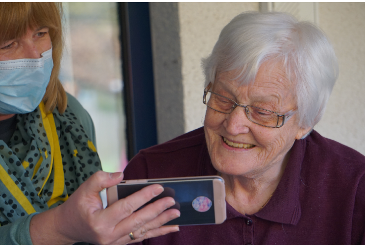 Elderly lady looking at a smartphone being held by carer wearing mask